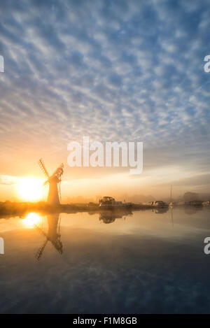 Atemberaubende Landschaft mit Windmühle und Fluss bei Sonnenaufgang am Sommermorgen Stockfoto