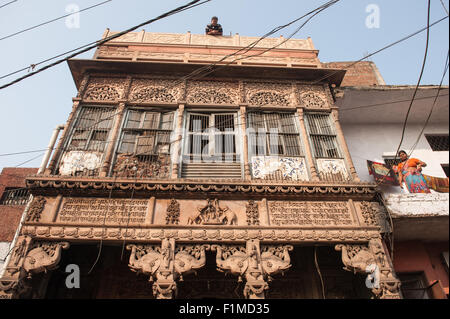 Agra, Uttar Pradesh, Indien. Reich geschnitzt aber verfallenen Tempel, Lakshmi, die Göttin von Fülle. Elefant-Schnitzereien und Frau im Haus nebenan, Mann auf dem Dach. Stockfoto