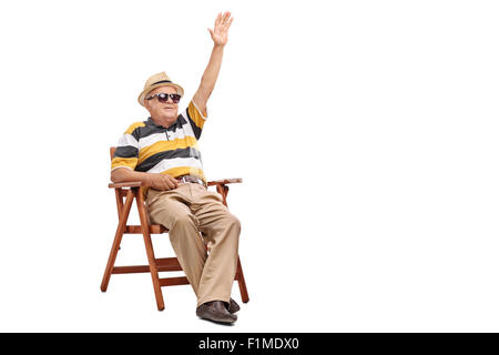 Senior Herr sitzt auf einem hölzernen Stuhl und winken für jemanden mit seiner Hand isoliert auf weißem Hintergrund Stockfoto