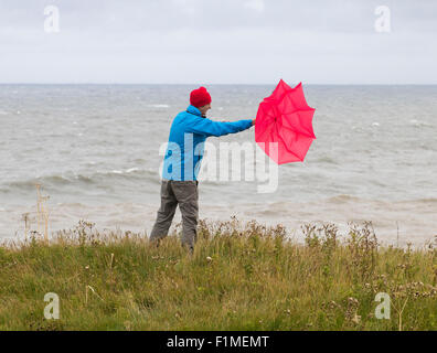 Mann mit rotem Regenschirm an windigen/stürmischen Tagen. VEREINIGTES KÖNIGREICH Stockfoto