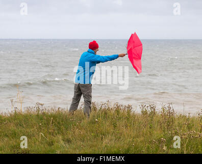 Mann mit rotem Regenschirm an windigen/stürmischen Tagen. VEREINIGTES KÖNIGREICH Stockfoto