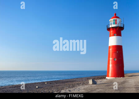 Ein rot-weißen Leuchtturm auf dem Meer unter strahlend blauem Himmel. Fotografiert in der Nähe von Westkapelle in Zeeland, Niederlande. Stockfoto