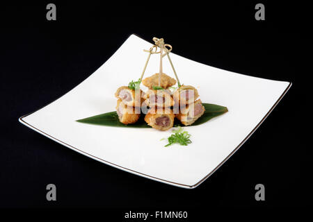 Panierte Fisch mit Gemüse in weißer Teller auf schwarzem Hintergrund Stockfoto