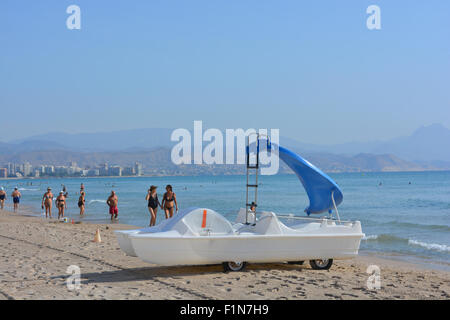 Ein Tretboot Boot mit Wasser gleiten zu mieten am Strand von Campello, mit frühen Morgen Wanderer, Alicante, Spanien. Stockfoto