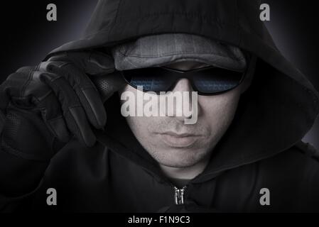 Hacker in einer Sonnenbrille, schwarze Lederhandschuhe und Haube Gesicht Closeup. Sonnenbrille Computertastatur widerspiegelt. Cyber-Angriff-Thema. Stockfoto