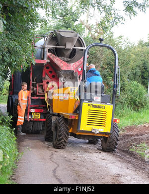 Entladen ein konkreten LKW in einen schmalen Feldweg in einen kleinen Bauherren-Kipper für die Platzierung auf einem Bauernhof Stockfoto