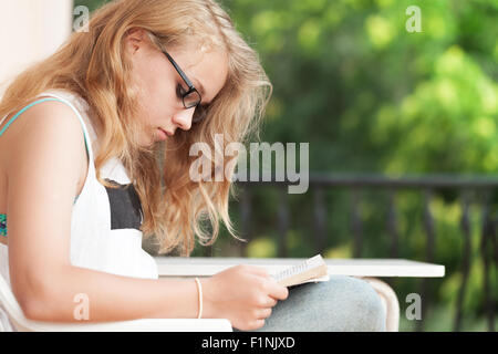 Blonde kaukasische Teenager-Mädchen auf dem Balkon sitzt und ein Buch lesen Stockfoto