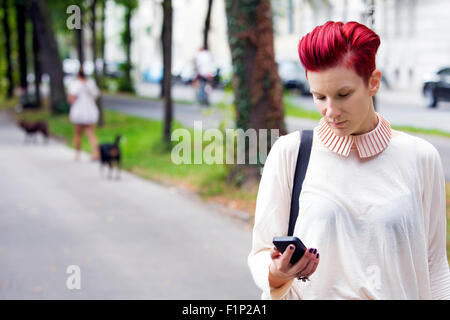 rothaarige Frau draußen und SMS auf dem Handy Stockfoto
