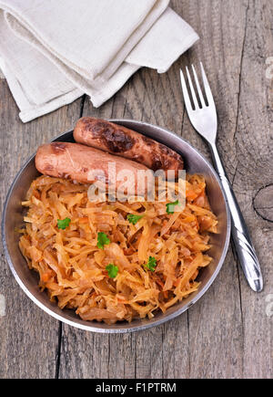 Eintopf von Kraut mit gegrillten Würstchen auf hölzernen Hintergrund, Ansicht von oben Stockfoto