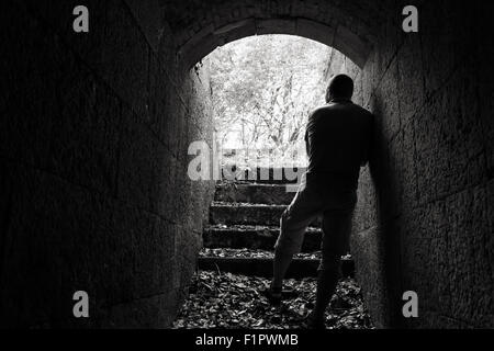 Junger Mann steht im dunklen Stein-Tunnel mit glühenden Ende, schwarz / weiß Foto Stockfoto