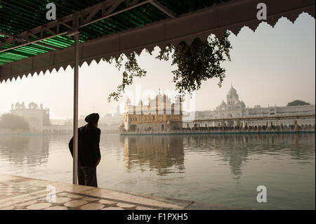 Amritsar, Punjab, Indien.  Der Goldene Tempel - Harmandir Sahib - im Morgengrauen mit einer alten Sikh seine Füße im heiligen Wasser Baden. Stockfoto