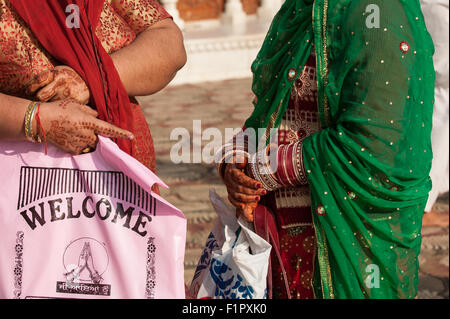 Amritsar, Punjab, Indien. Zwei Frauen, ihre Hände mit Henna komplizierten Mustern bemalt. Man hält eine rosa Plastiktüte mit "Willkommen" Englisch und Punjabi schriftlich. Stockfoto