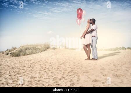 Süße junge Couple Standing am Strand mit Ballons an einem sehr sonnigen Tag. Stockfoto