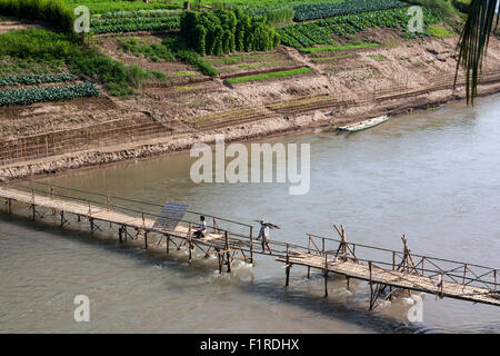 Arbeiter balanciert auf einem einpoligen wie er eine Bambusbrücke über den Nam Khan Fluss unten Luang Prabang, Laos beendet Stockfoto