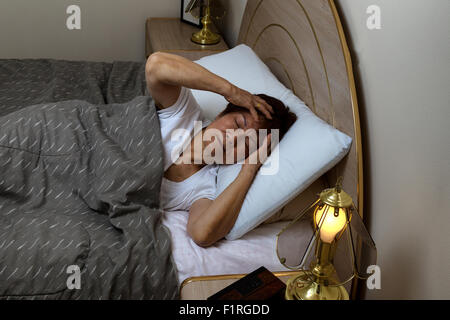 Ältere Frau im Bett, hielt ihren Kopf bei Schmerzen während der Nachtzeit. Schlaflosigkeit-Konzept. Stockfoto