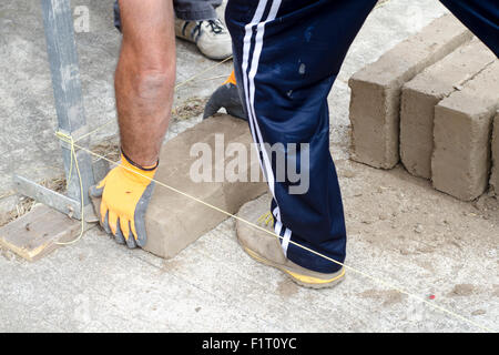 männliche Hand mit Handschuh Positionierung der ersten Ziegelbau Wand harter Arbeiter Stockfoto