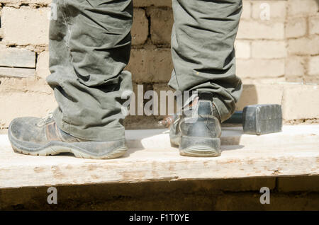 Nahaufnahme eines männlichen Stiefel schmutzige Arbeit auf der Baustelle und einem hammer Stockfoto