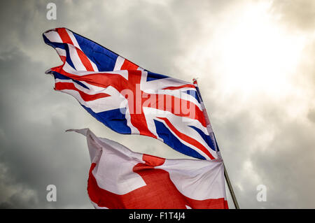 Englische Union Jack und St. George Fahne flattert im Wind gegen grauen bewölktem Himmel Stockfoto