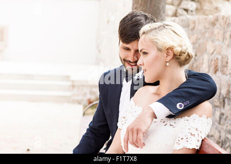 Glückliche Braut und Bräutigam sitzen auf Bank Stockfoto