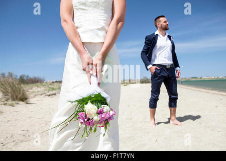 Braut am Strand halten Bukett, Bräutigam im Hintergrund Stockfoto