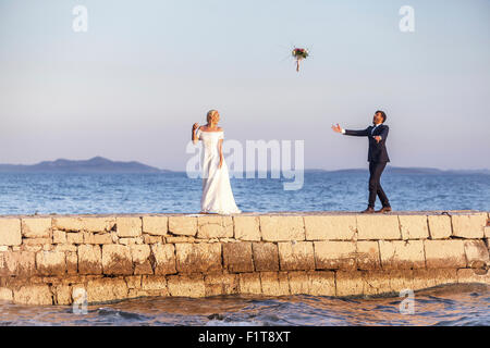 Braut und Bräutigam am Pier werfen Blumenstrauß in Luft Stockfoto