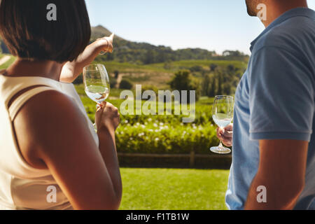 Junges Paar im Urlaub mit einem Glas Wein, mit Frau zeigt entfernt am Weinberg, zeigen etwas zu ihrem Freund. Stockfoto