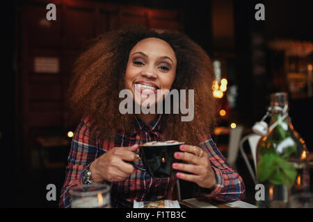 Porträt der jungen Frau Kaffee trinken. Afrikanische Frau sitzen im Café hält eine Tasse Kaffee, Blick auf die Kamera zu Lächeln. Stockfoto