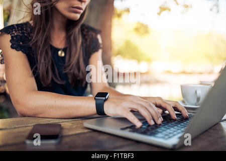 Junge Frau trägt Smartwatch mit Laptop-Computer. Frauen arbeiten am Laptop in einem Straßencafé. Stockfoto