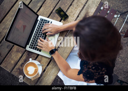 Draufsicht der junge Frau trägt eine Smartwatch auf ihrem Laptop in einem Café arbeiten. Top Aussicht Schuss von weiblichen sitzen an einem Tisch wi Stockfoto