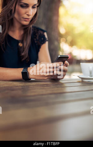 Bild der jungen weiblichen lesen eine SMS-Nachricht auf ihr Smartphone zugeschnitten. Frau mit Smartphone in ein Café im Freien. Stockfoto