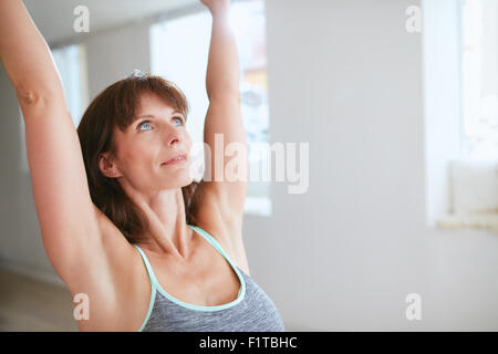 Schuss von Yoga zu praktizieren Reife Frau mit ihren Armen angehoben und auf der Suche nach oben im Fitness-Studio hautnah. Fitness weiblichen Krieger posiere ich Stockfoto
