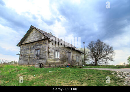 Vorderansicht des Altbaus Holzhaus im Wiesenbereich zwischen toten Bäumen, auf blauen Wolkenhimmel Hintergrund allein stehend. Stockfoto