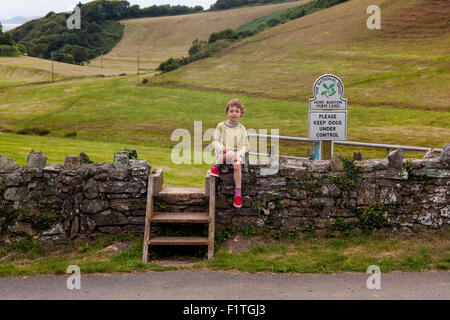 Sechs Jahre alter Junge sitzt auf einer Steinmauer, Hope Cove, Devon, England, Vereinigtes Königreich. Stockfoto