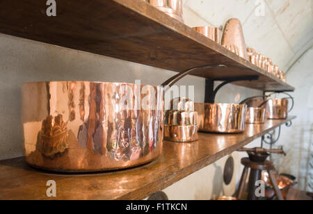 Ein Regal von glänzendem Kupfer Töpfe. Ein Küchenregal widmet sich die Anzeige der feinen alten bekleideten Kupfertöpfe und andere Küchenutensilien. Stockfoto