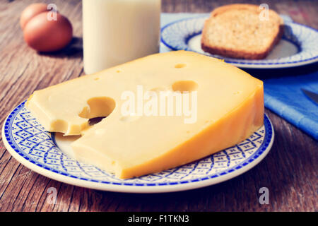 Nahaufnahme von ein Stück Schweizer Käse in einen Teller, eine Flasche mit Milch, einige braunen Eiern und einen Teller mit etwas Toast auf einem rustikalen Holz Stockfoto