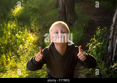 Gut aussehend wenig glückliches lächelndes Kind (junge) Wandern und Spaß in den grünen Wald (Park), Daumen hoch Stockfoto