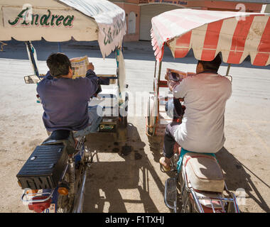 Warten auf Benutzerdefiniert. Zwei motor-Dreirad-Fahrer lesen Zeitungen während des Wartens auf Kunden. Ticul, Yucatan, Mexiko Stockfoto