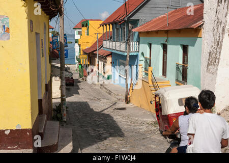 Motorrad- und Jeep fahren Sie Calle de 10 Novembre vorbei an bunten Häusern in Flores, Guatemala. Lake Petén Itzá sichtbar über Stockfoto