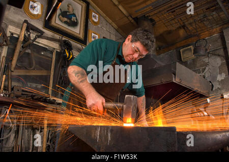 Schmied Simon Grant-Jones Hämmern heiße Metall mit Funken fliegen, in seiner Schmiede, wo er ein Handwerker-metalworker.a UK ist Stockfoto