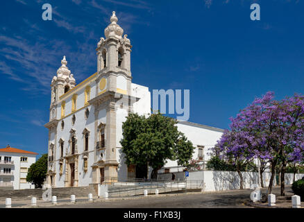 Faro, die Igreja Carmo Barockkirche mit Jacaranda-Bäume in Blüte, Algarve, Portugal Stockfoto