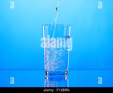 Gießen Wasser in Glas auf blauem Hintergrund. Stockfoto