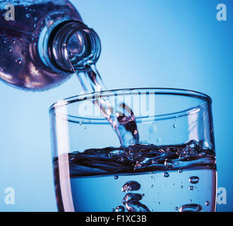 Gießen Wasser aus der Flasche ins Glas auf blauem Hintergrund Stockfoto