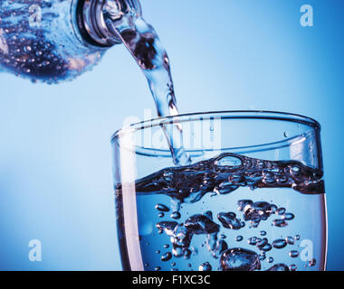 Gießen Wasser aus der Flasche ins Glas auf blauem Hintergrund Stockfoto