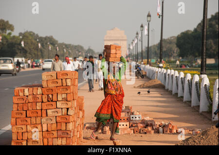 Delhi, Indien. Frau Arbeiter tragen 8 acht Ziegel auf dem Kopf aus einem Haufen von Steinen an der Seite von der Straße in der Nähe das India Gate. Stockfoto