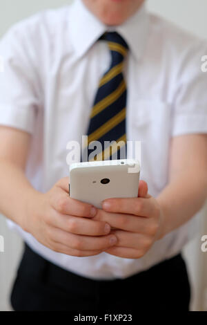 Ein Schulkind in Uniform mit seinem Mobiltelefon (SMS) UK Stockfoto