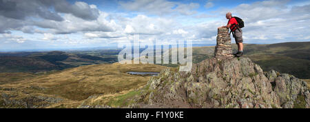 Walker am Gipfel Cairn und OS Triglyzerid Punkt auf Platz fiel, Nationalpark Lake District, Cumbria, England, UK. Stockfoto