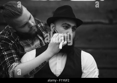 Barbier rasiert ein bärtigen Mannes Stockfoto