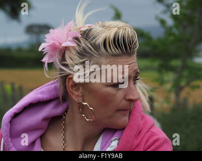 windgepeitschten Frau mit rosa gefälschte Blume in Flasche blondes Haar an der berühmten jährlichen Reisende Raffungen am Appleby Horse Fair, Cumbria, England UK Stockfoto