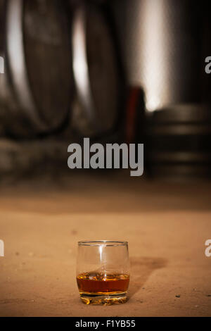 Glas gefüllt mit Whisky, ordentlich ohne Eis, auf Boden in Brennerei mit Fässern im Hintergrund. Stockfoto