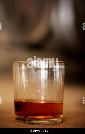 Glas gefüllt mit Whisky, ordentlich ohne Eis, auf Boden in Brennerei mit Fässern im Hintergrund. Stockfoto